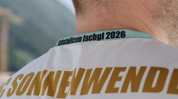 Ein Mann trägt ein T-Shirt mit dem Namen "Sonnenwende" und einem Aufdruck für den "KristallCup Ischgl 2026". Die Atmosphäre wirkt sportlich und enthusiastisch.