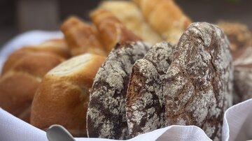 A basket full of fresh rolls and breads, along with a small bowl of hummus. An edible flower decorates the hummus bowl.