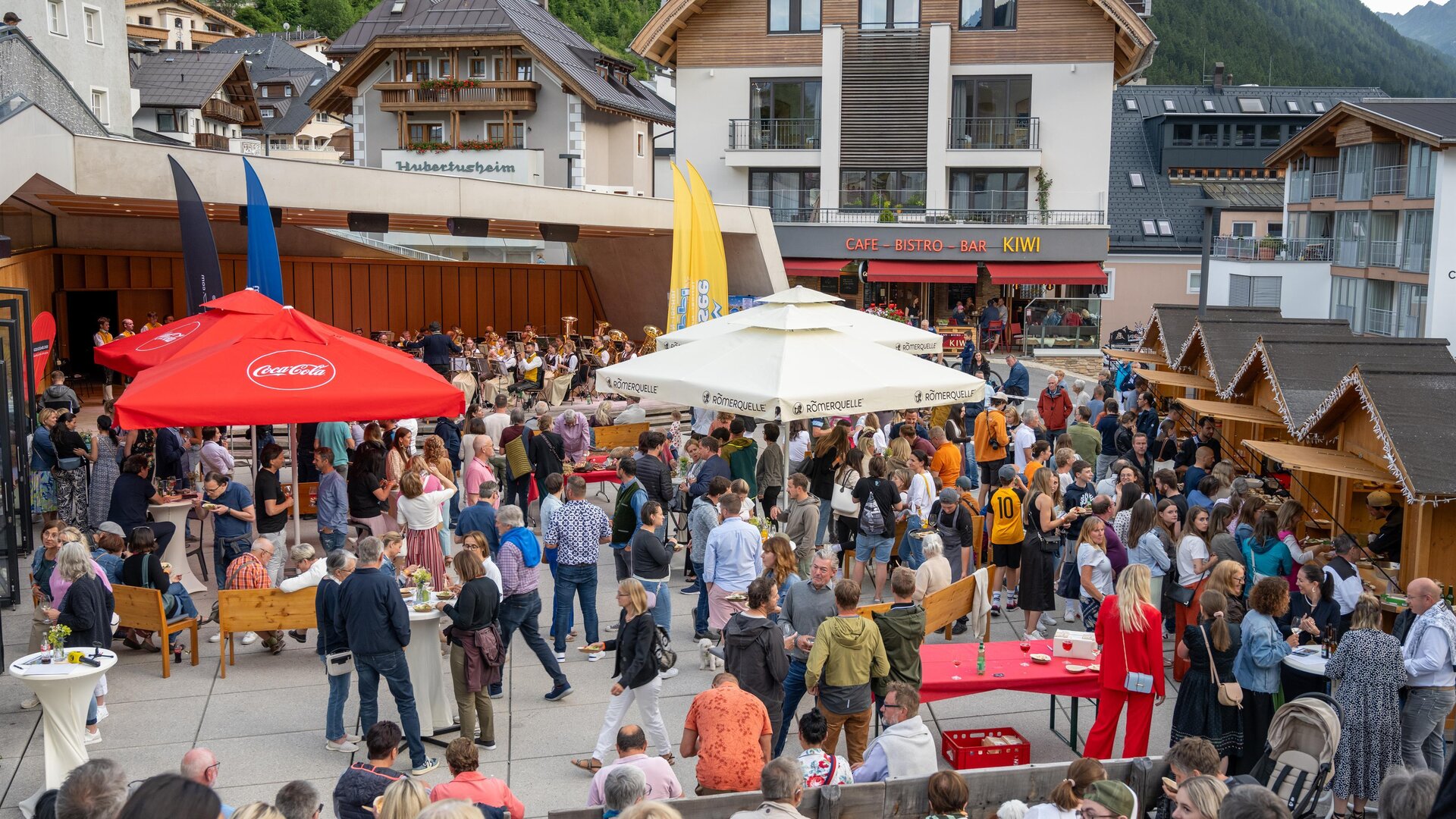 A bustling square with many people participating in a festival. Surrounded by stalls and buildings, the atmosphere radiates joy and camaraderie.