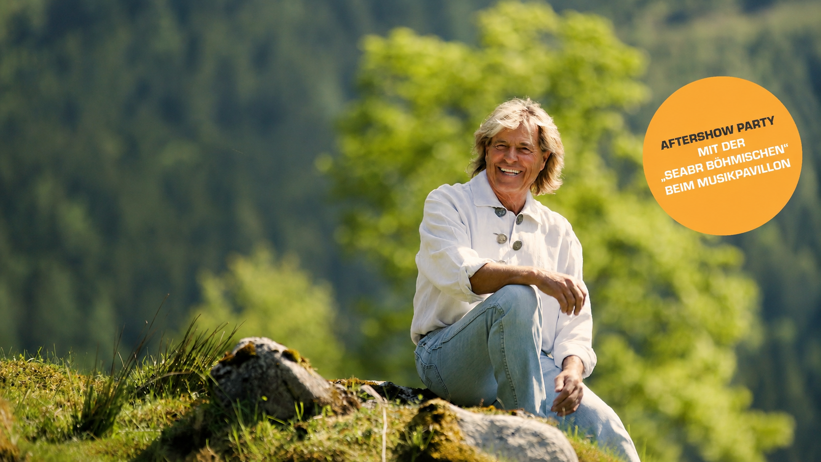 A smiling man is sitting on a rock in nature, surrounded by green trees. In the background, there is an event notice for an aftershow party.