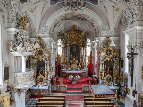 Eine prächtige Kirche mit reich verzierten Wänden und einem kunstvollen Altar. Der Innenraum ist lichtdurchflutet und strahlt eine spirituelle Atmosphäre aus.
