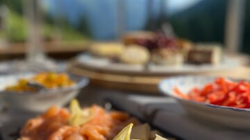 An attractively arranged plate with various types of fish, garnished with a slice of lemon. In the background, there is a beautiful landscape with mountains and a clear blue sky.