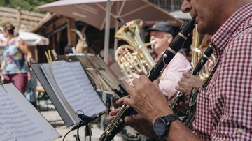 Eine Band spielt im Freien unter Sonnenschirmen. Der Mann vorne spielt Klarinette und trägt eine karierte Bluse.