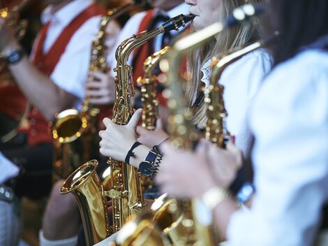 A group of musicians is playing saxophone. They are wearing traditional clothing and focusing on their instruments.