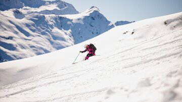 A skier is gliding down a snow-covered slope in the mountains. The sky is clear and the mountains are covered with snow.