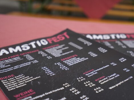 Ein Restaurant-Menü mit der Aufschrift "SAMSTIÖFEST". Die Karte bietet verschiedene Getränke und Speisen an.