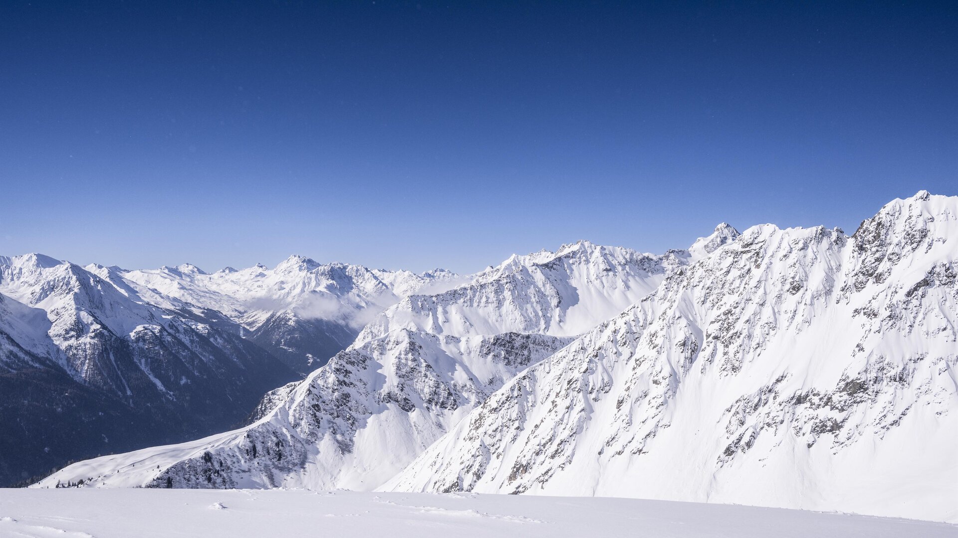 Eine beeindruckende Berglandschaft mit schneebedeckten Gipfeln und klarem blauen Himmel. Die schroffen Felsen und tiefen Täler schaffen eine majestätische Aussicht.