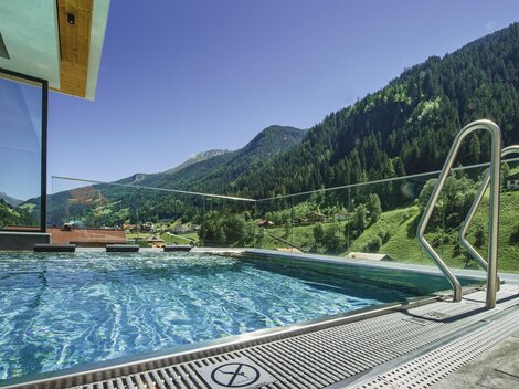 A modern infinity pool with clear water and a view of green mountains. The surroundings are peaceful and inviting.