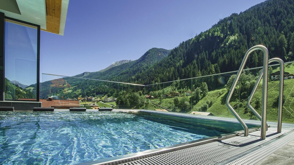 A modern infinity pool with clear water and a view of green mountains. The surroundings are peaceful and inviting.