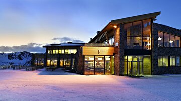 Ein modernes Gebäude in den Bergen, umgeben von Schnee. Der Sonnenuntergang zaubert eine warme Atmosphäre.