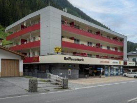 Ein modernes Gebäude mit mehreren Etagen und Balkonen. Unten befindet sich eine Raiffeisenbank und Geschäfte.