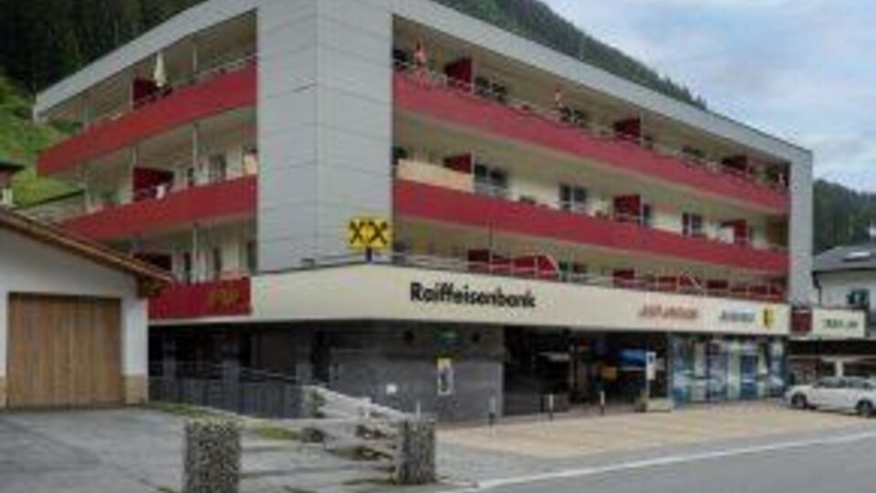 Ein modernes Gebäude mit mehreren Etagen und Balkonen. Unten befindet sich eine Raiffeisenbank und Geschäfte.