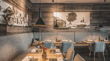 A cozy restaurant with wooden walls and stylish furniture. The tables are set with cutlery and flower decorations.