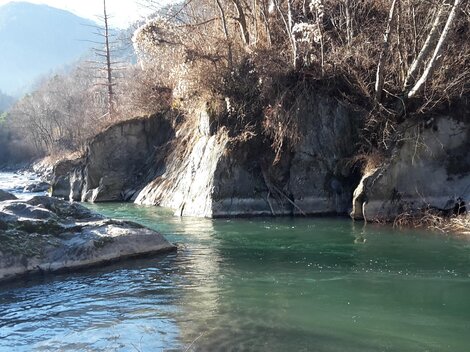 A calm river flows between rocky shores. In the background, wooded hills are visible.