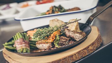 Ein köstliches Gericht auf einer Eisenpfanne, das zartes Fleisch mit frischem Gemüse kombiniert. Dazu sind würzige Kräuter und eine belebende Sauce angerichtet.