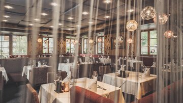 Ein gemütliches Restaurant mit eleganten Tischen und stimmungsvollem Licht. Die großen Fenster bieten Blick ins Freie und schaffen eine einladende Atmosphäre.