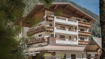 Ein charmanter Berghotel mit mehreren Balkonen und Holzverzierungen. Umgeben von einer malerischen Naturkulisse.