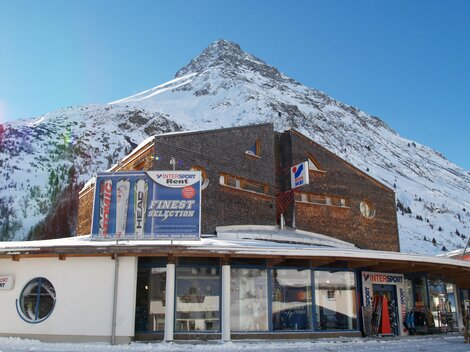 A modern building in front of a snow-covered mountain. The clear sky and winter landscape create a picturesque view.
