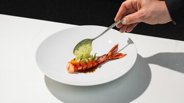 A chef decorates a plate with a shrimp and a green sauce. The white plate highlights the colors of the dish.