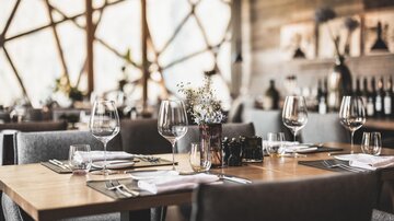 An elegant restaurant with wooden tables and stylish chairs. The tables are lovingly decorated with glassware and flowers.