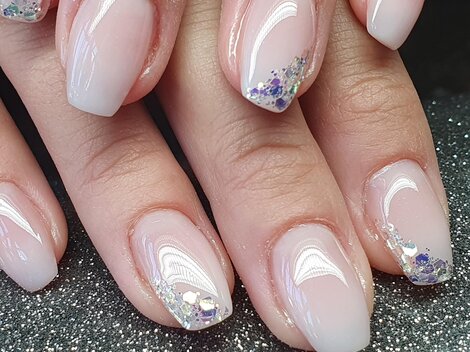 Beautiful manicure with delicate pink nails and glittering accents. The nails are neatly shaped and shine elegantly.