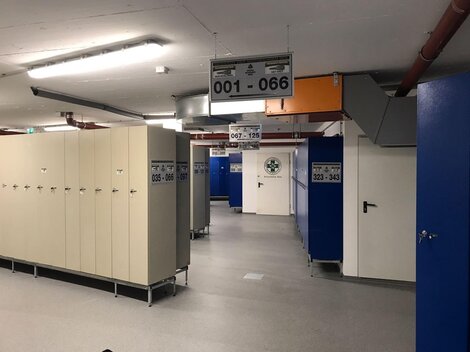 A modern changing area with numerous lockers. The walls are painted blue and the lighting is bright.