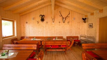A cozy wooden room with rustic tables and benches. Hunting trophies hang on the walls, and there are large windows that provide daylight.