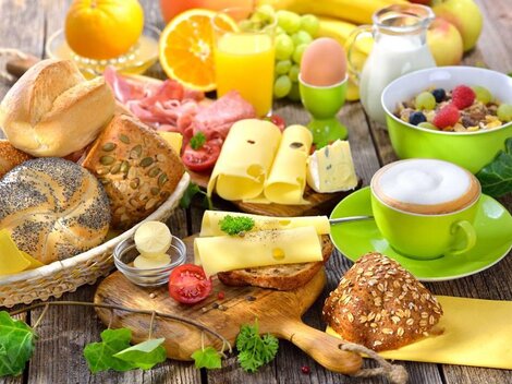 A hearty breakfast with various types of bread, colorful fruit, and drinks. Additionally, there is cheese and yogurt in appetizing bowls.