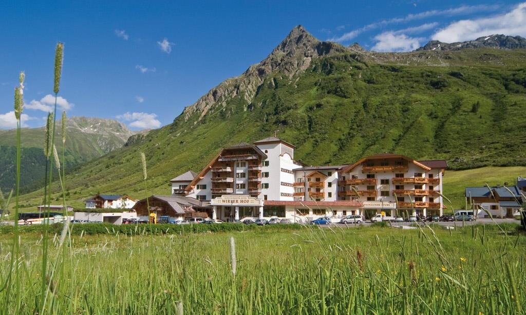 A beautiful hotel in the mountains with green meadows and a blue sky. The surrounding landscape is picturesque and inviting.