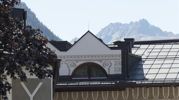 A cable car floats over a traditional inn in the mountains. In the background, the peaks of the mountains are visible.