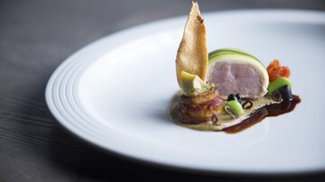 An artistically arranged dish on a white plate. It features tender pieces of meat, decorative side dishes, and an appealing presentation.