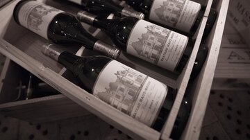 A box with several wine bottles that are artistically labeled. The bottles lie in wooden boxes, surrounded by shadows and a rustic ambiance.