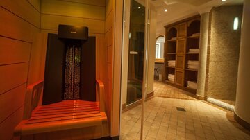 A cozy wellness area with an infrared bench and large shelves filled with towels. Soft lighting and warm colors create a relaxing atmosphere.