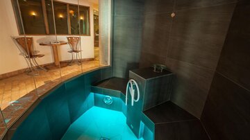 A modern steam bath with softly lit water and stylish tiles. In the background, a table and chairs can be seen.