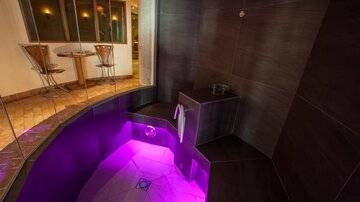 A luxurious wellness area with a round, softly lit pool. The walls are dark, and there are modern seating options in the background.